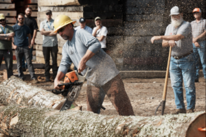 Justin Gundlach cutting a log while his father Henry Gundlach stands ready to assist. 